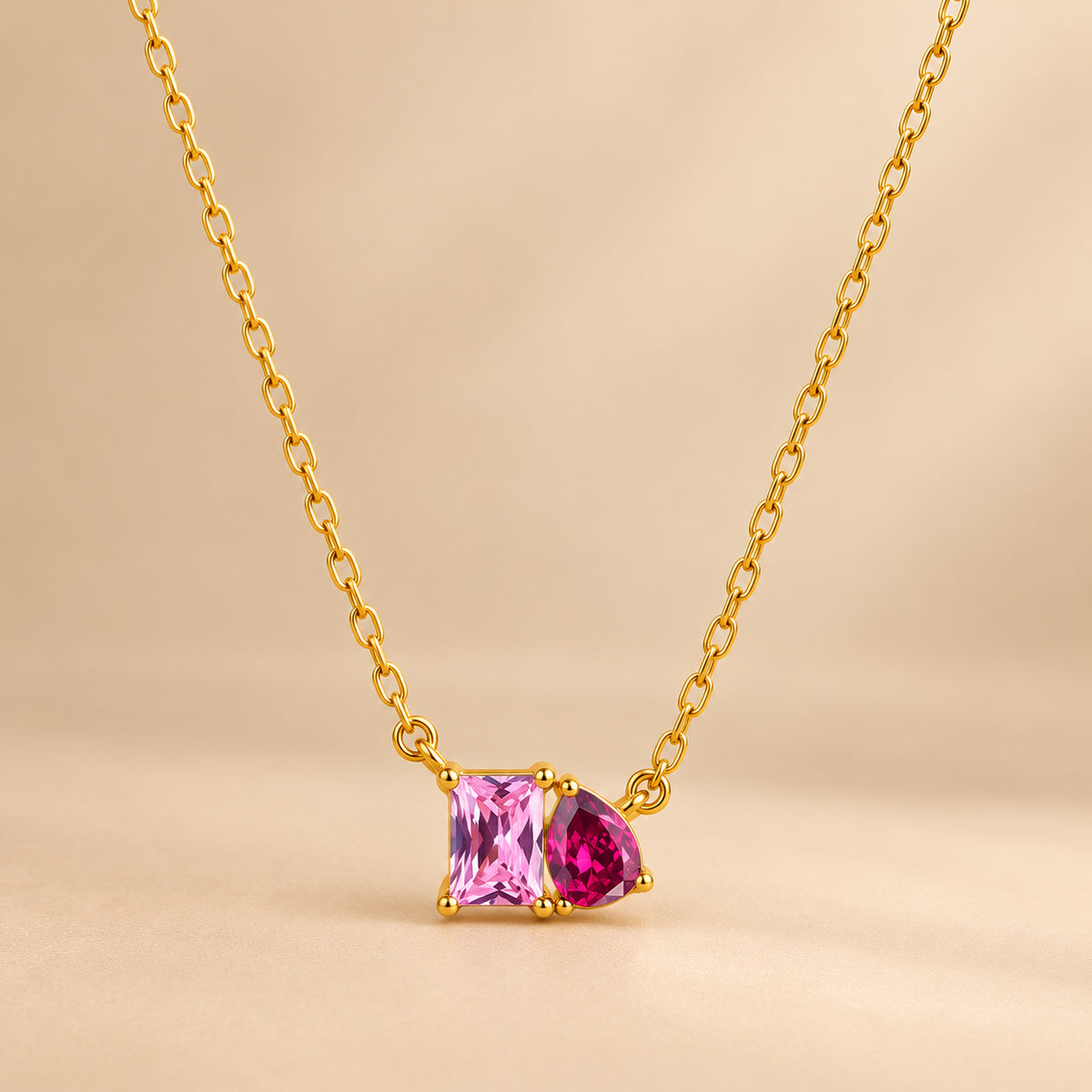 Colar CLARA dourado com dois detalhes coloridos rosa e vermelho sobre fundo bege