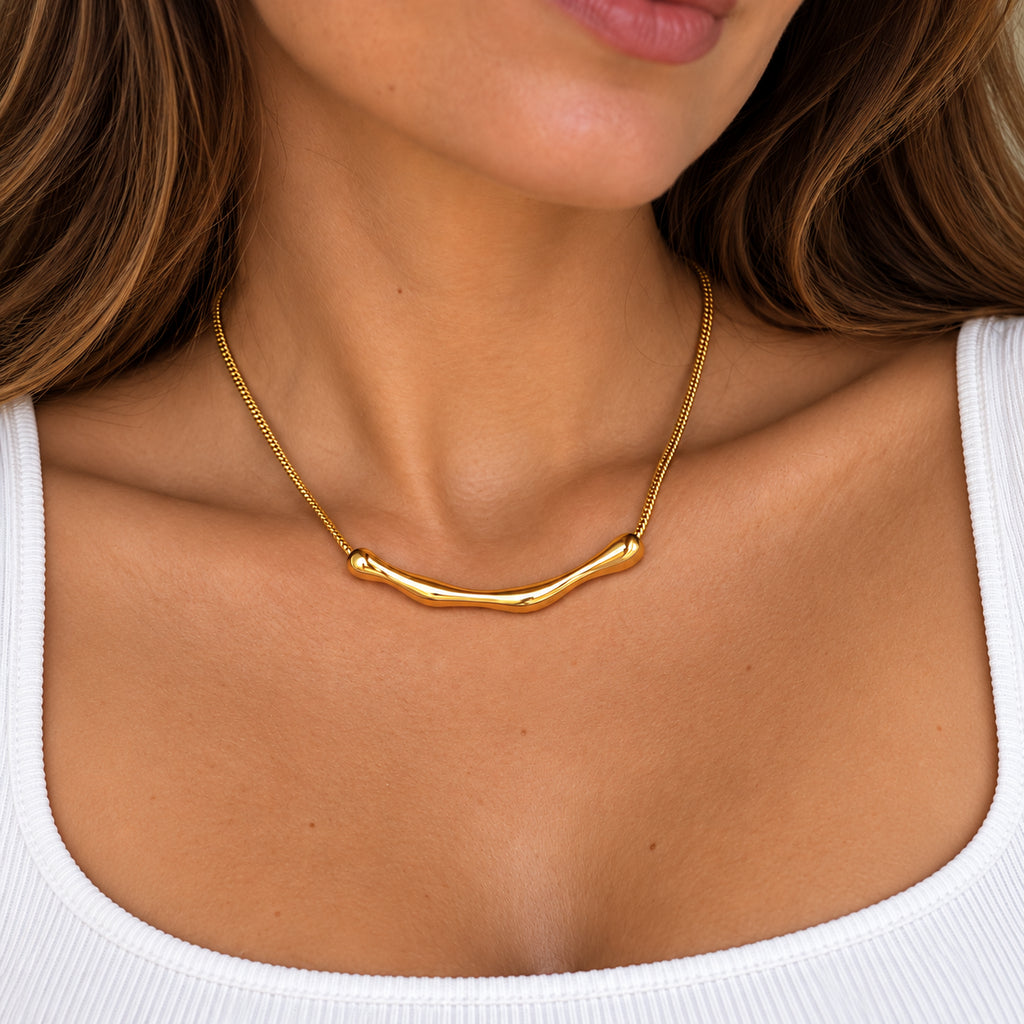 Colar MIRA dourado em uso no pescoço, com design minimalista e elemento central curvo