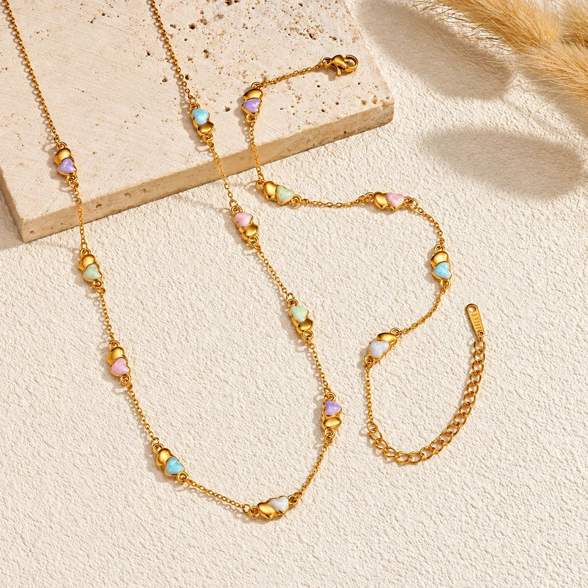 Conjunto CELINE com colar e pulseira em aço inoxidável, acabamento dourado e corações coloridos, imagem principal