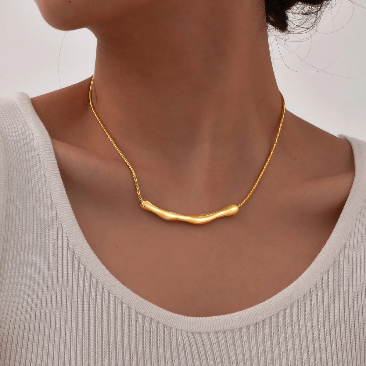 Colar MIRA dourado em uso no pescoço feminino, mostrando o comprimento e a forma do elemento central